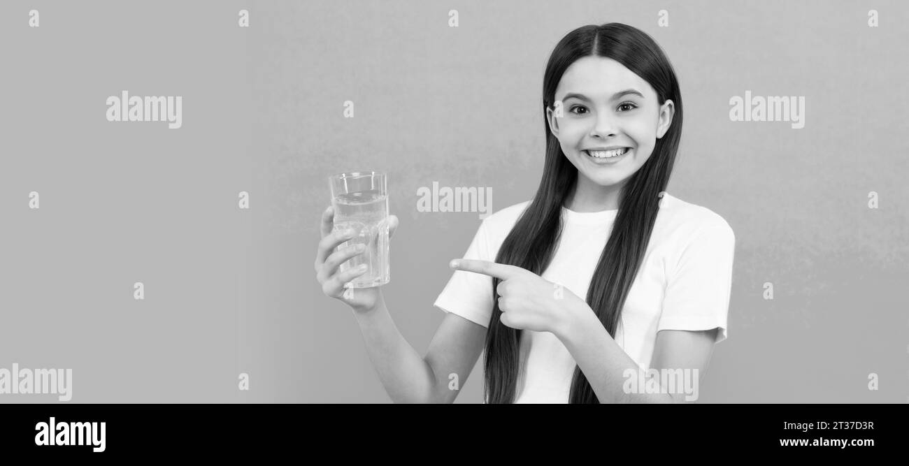 enfant heureux boire un verre d'eau pour rester hydraté et garder l'équilibre quotidien de l'eau, pointant du doigt. Bannière de l'enfant fille avec verre d'eau, studio portra Banque D'Images