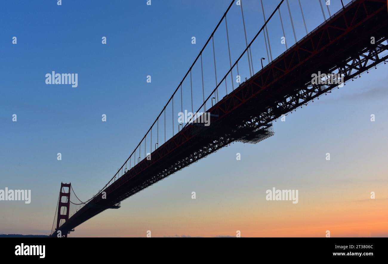 Vue grand format d'un bateau pendant qu'il navigue sous le célèbre et beau Golden Gate Bridge au coucher du soleil. Banque D'Images