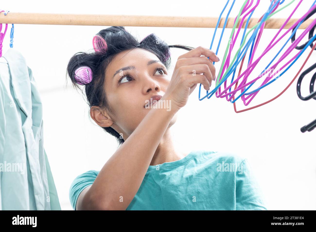 Une jeune femme avec des bigoudis dans les cheveux accroche du linge mouillé sur des cintres Banque D'Images