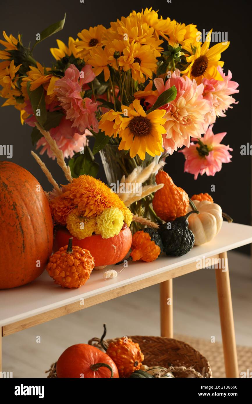 Composition d'automne avec de belles fleurs et citrouilles sur la table de console près du mur gris foncé Banque D'Images