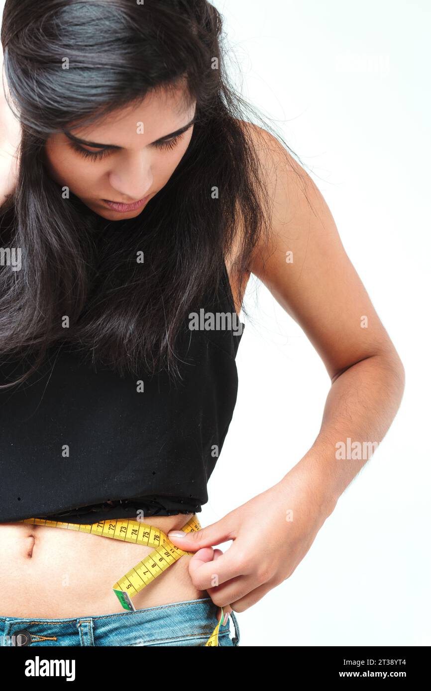 moment d'auto-réflexion, comme une femme aux cheveux longs et fluides prend des mesures précises de sa taille. Son haut noir et son Jean fournissent un contras austère Banque D'Images