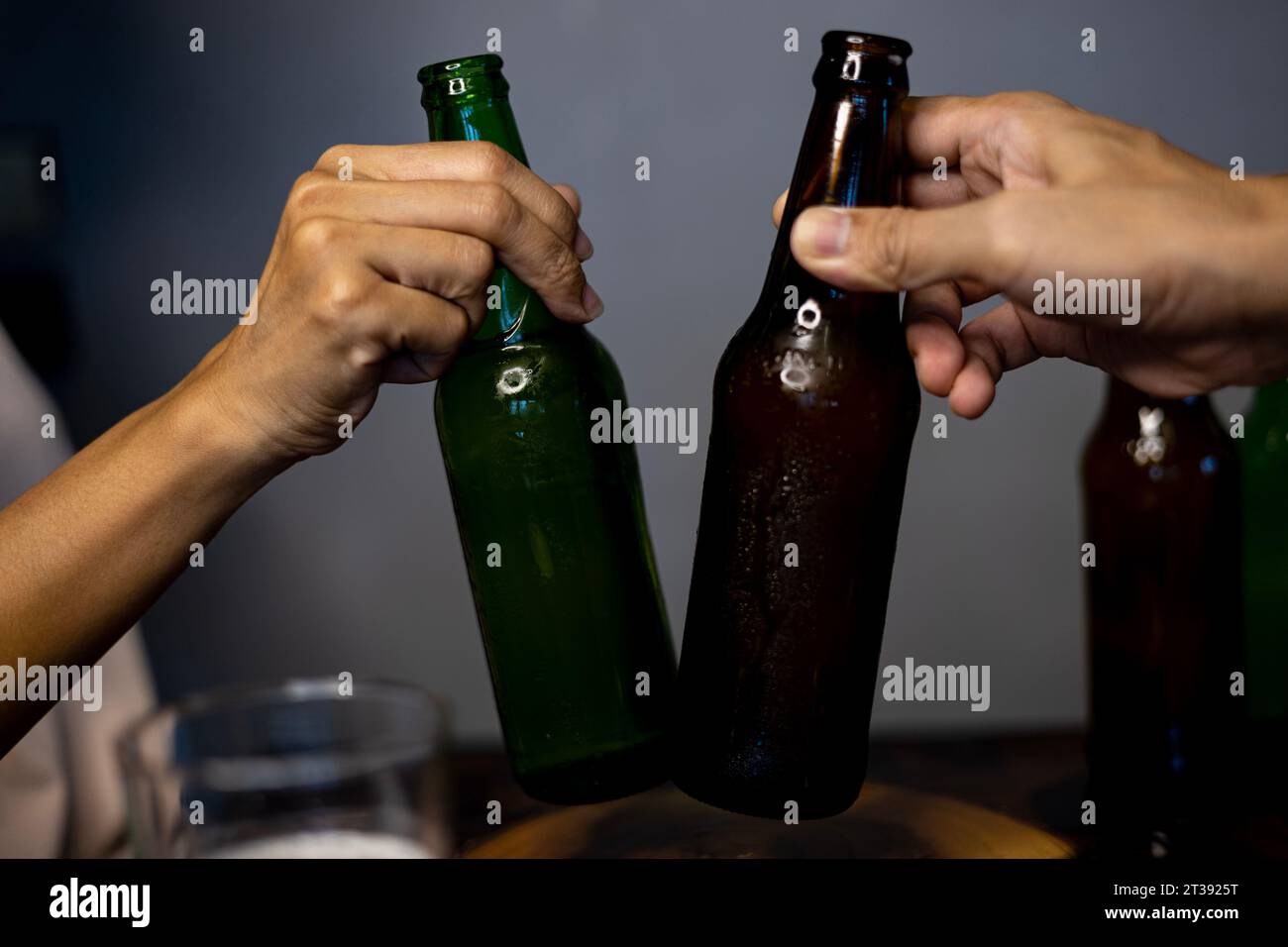 Deux amis grillant avec une bouteille de bière légère. Mains soulevant deux bouteilles de bière et heureux de profiter du temps de récolte ensemble à clinking verres à l'intérieur p Banque D'Images