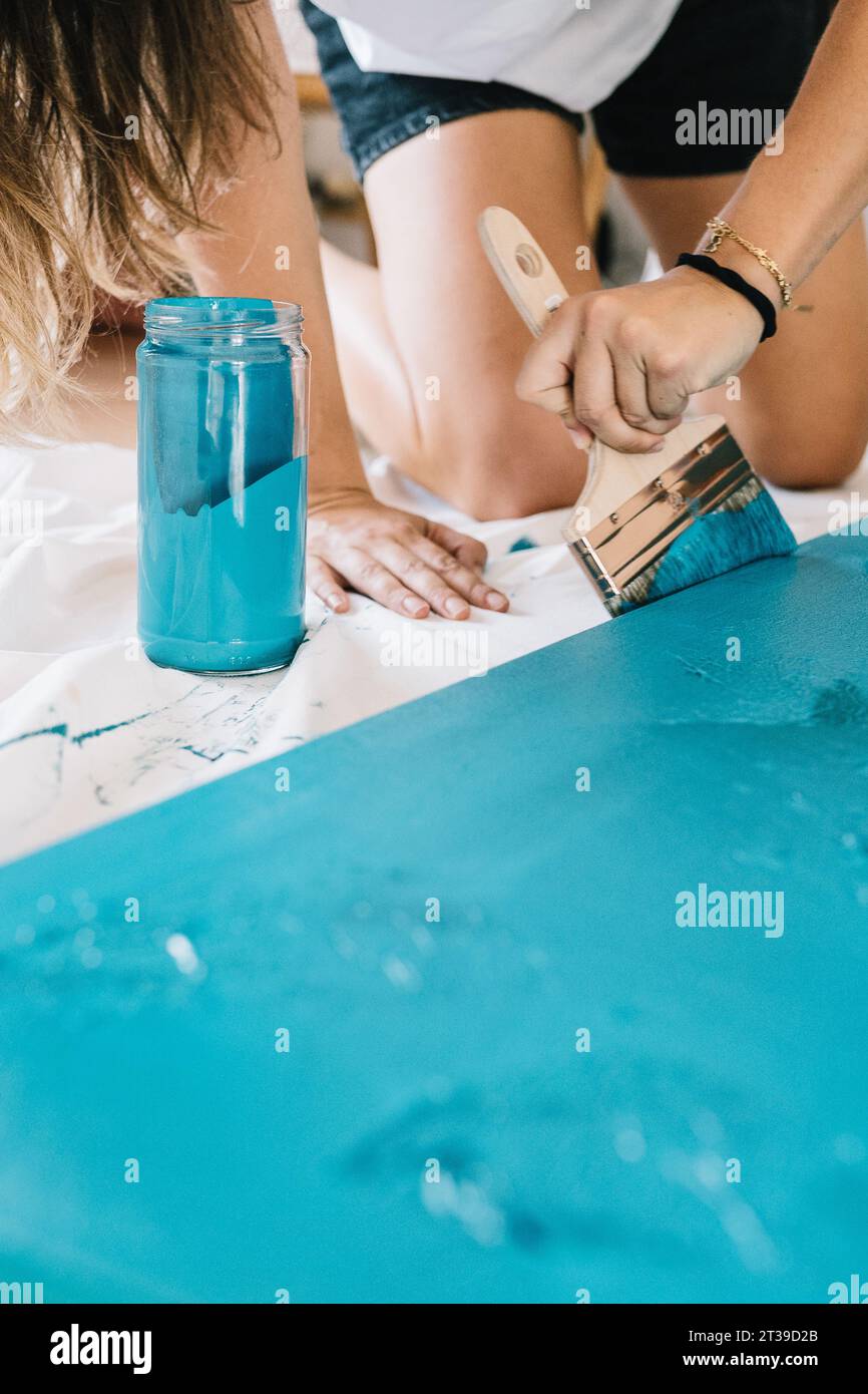 Recadrer peintre féminine méconnaissable à l'aide d'un pinceau tout en peignant la couleur bleue sur une planche de bois dans un studio créatif avec de la peinture brillante Banque D'Images