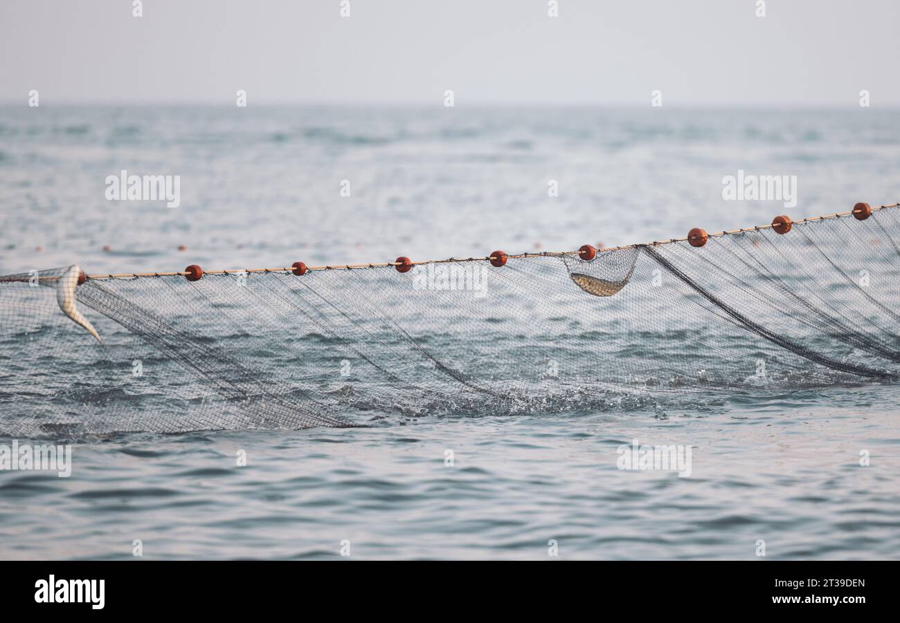 Vue panoramique de l'eau de mer ondulante éclaboussant filet de pêche avec corde attachée avec des flotteurs de liège rouge sur la journée ensoleillée de l'été contre un ciel sans nuages brouillé Banque D'Images