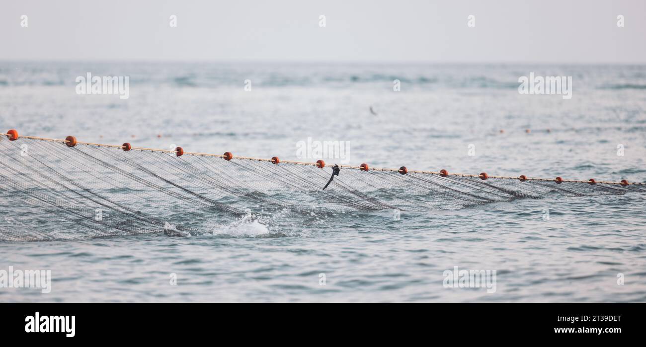 Vue panoramique de l'eau de mer ondulante éclaboussant filet de pêche avec corde attachée avec des flotteurs de liège rouge sur la journée ensoleillée de l'été contre un ciel sans nuages brouillé Banque D'Images
