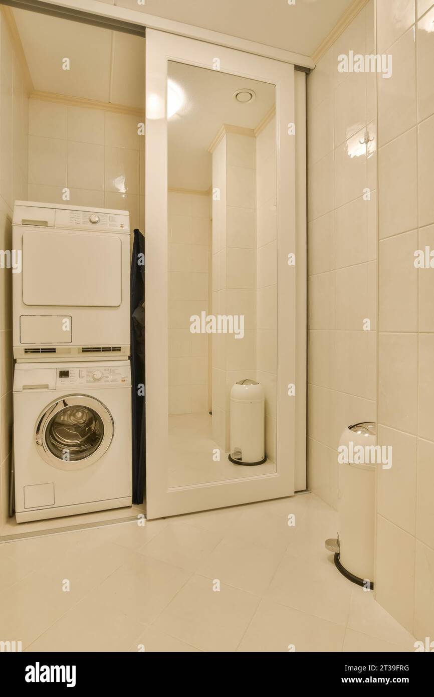 Lave-linge et sèche-linge par cabine de douche avec portes coulissantes dans une salle de bains blanche moderne à la maison Banque D'Images