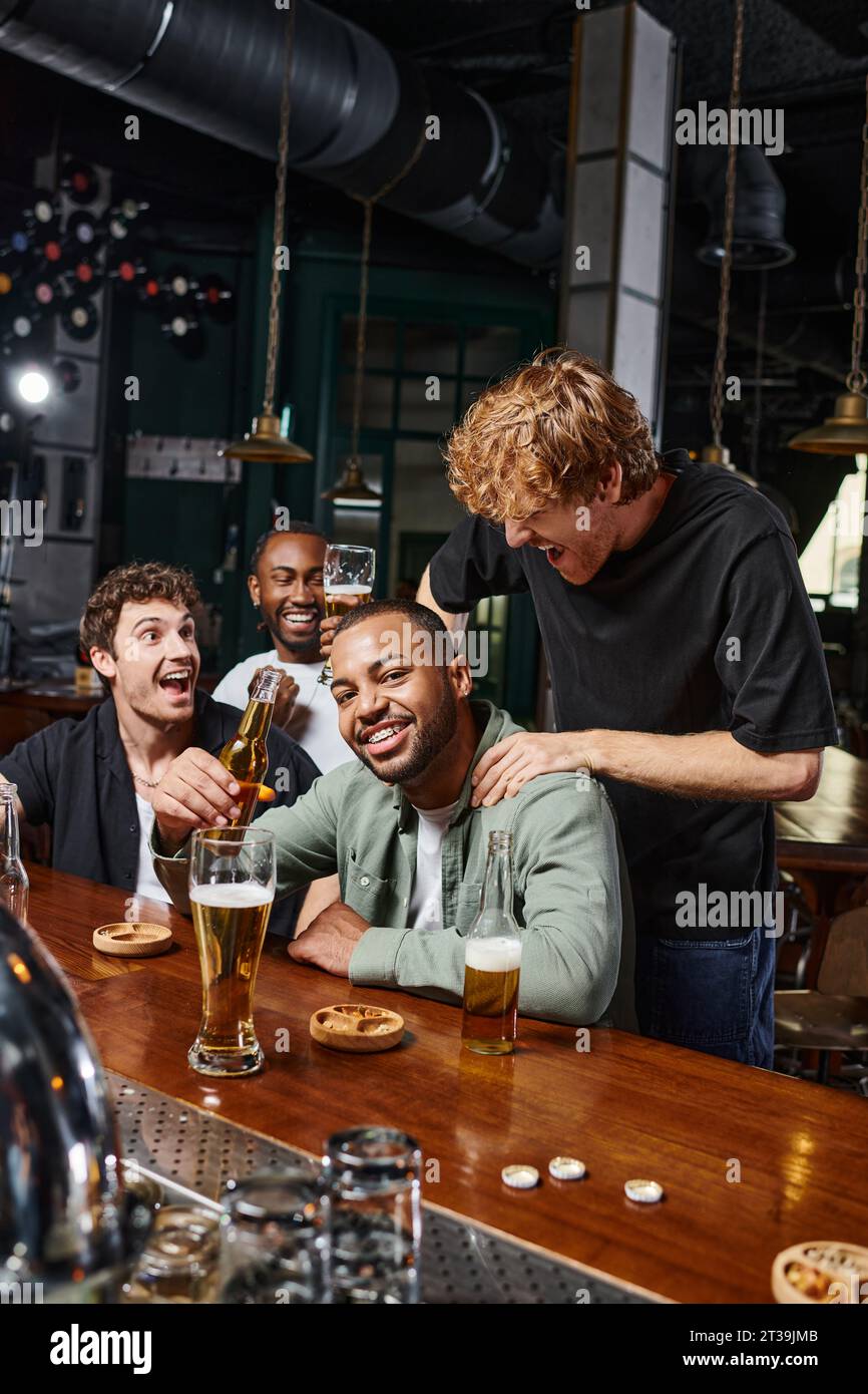 homme redhead touchant les épaules du marié afro-américain pendant la fête de célibataire, amitié masculine Banque D'Images