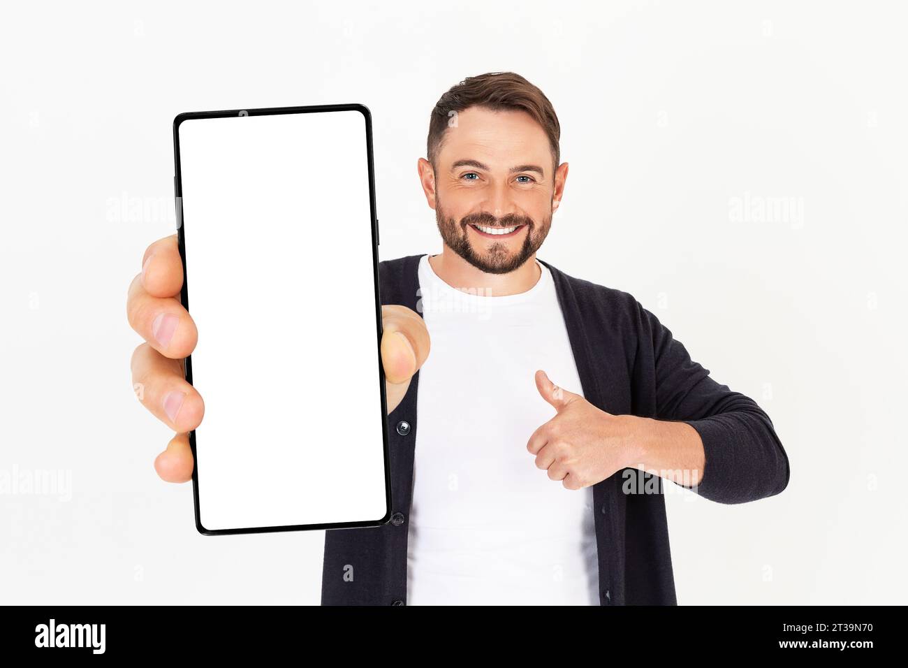 Beau jeune homme tenant une maquette de smartphone avec un écran vide et souriant sur un fond blanc. Célébrer le succès. Gadget avec espace vide pour Banque D'Images