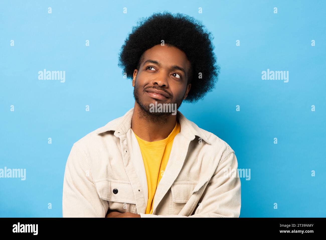 Homme afro-américain souriant pensant et regardant en arrière-plan de studio isolé de couleur bleu clair Banque D'Images