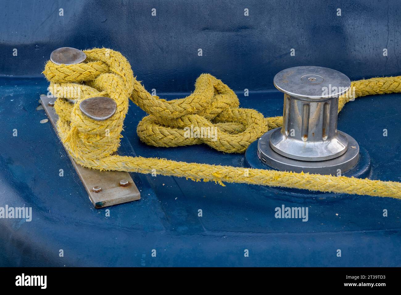 corde de yachting de couleur jaune faite rapidement attaché autour d'un taquet chromé avec un petit treuil en tôle également en chrome sur un pont de yacht à voile. Banque D'Images