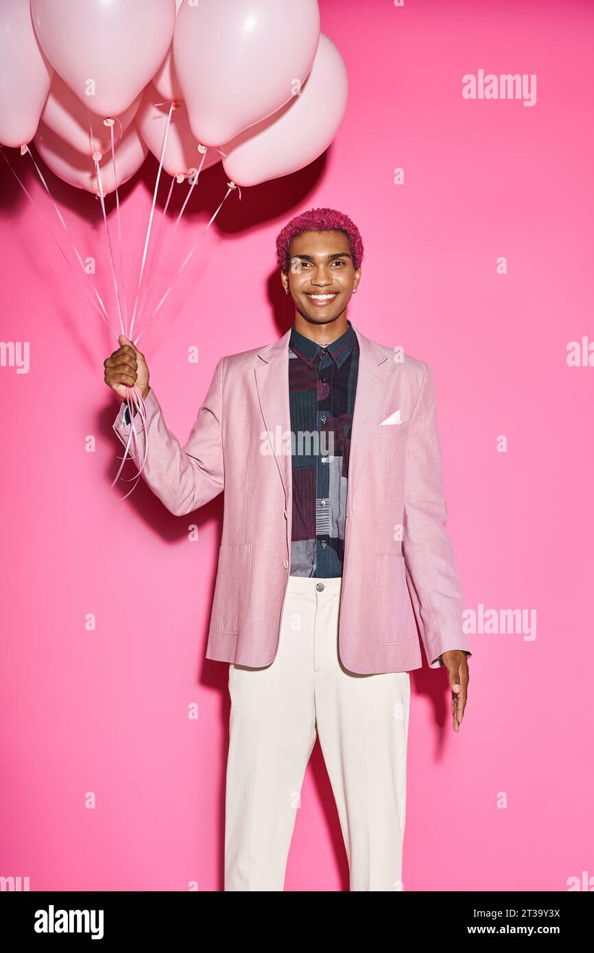 modèle masculin joyeux souriant heureux avec des ballons dans les mains et regardant la caméra sur fond rose Banque D'Images