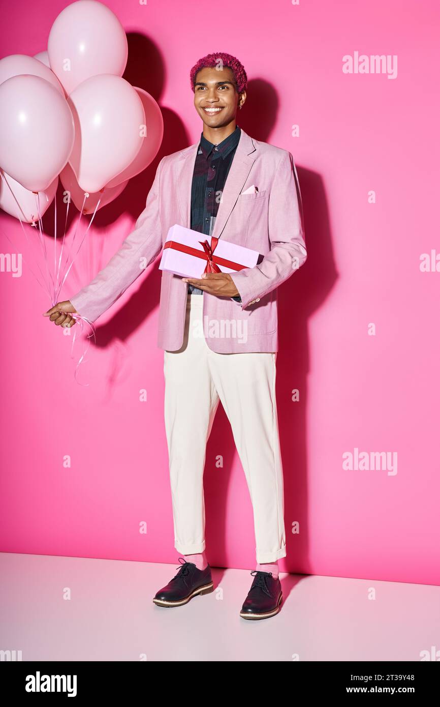 beau modèle masculin afro-américain posant anormalement avec des ballons et présent dans les mains Banque D'Images