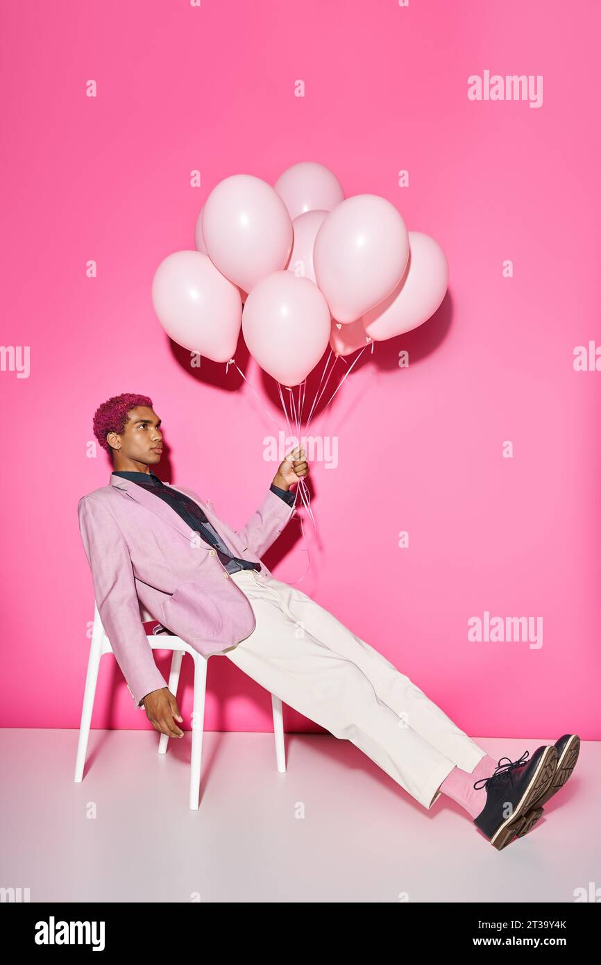 beau jeune modèle masculin posant anormalement avec des ballons à la main sur fond rose, comme poupée Banque D'Images
