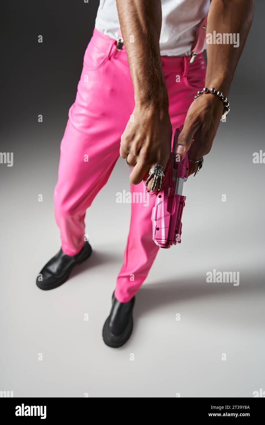 vue recadrée du modèle masculin afro-américain en pantalon rose avec bretelles posant avec pistolet jouet Banque D'Images