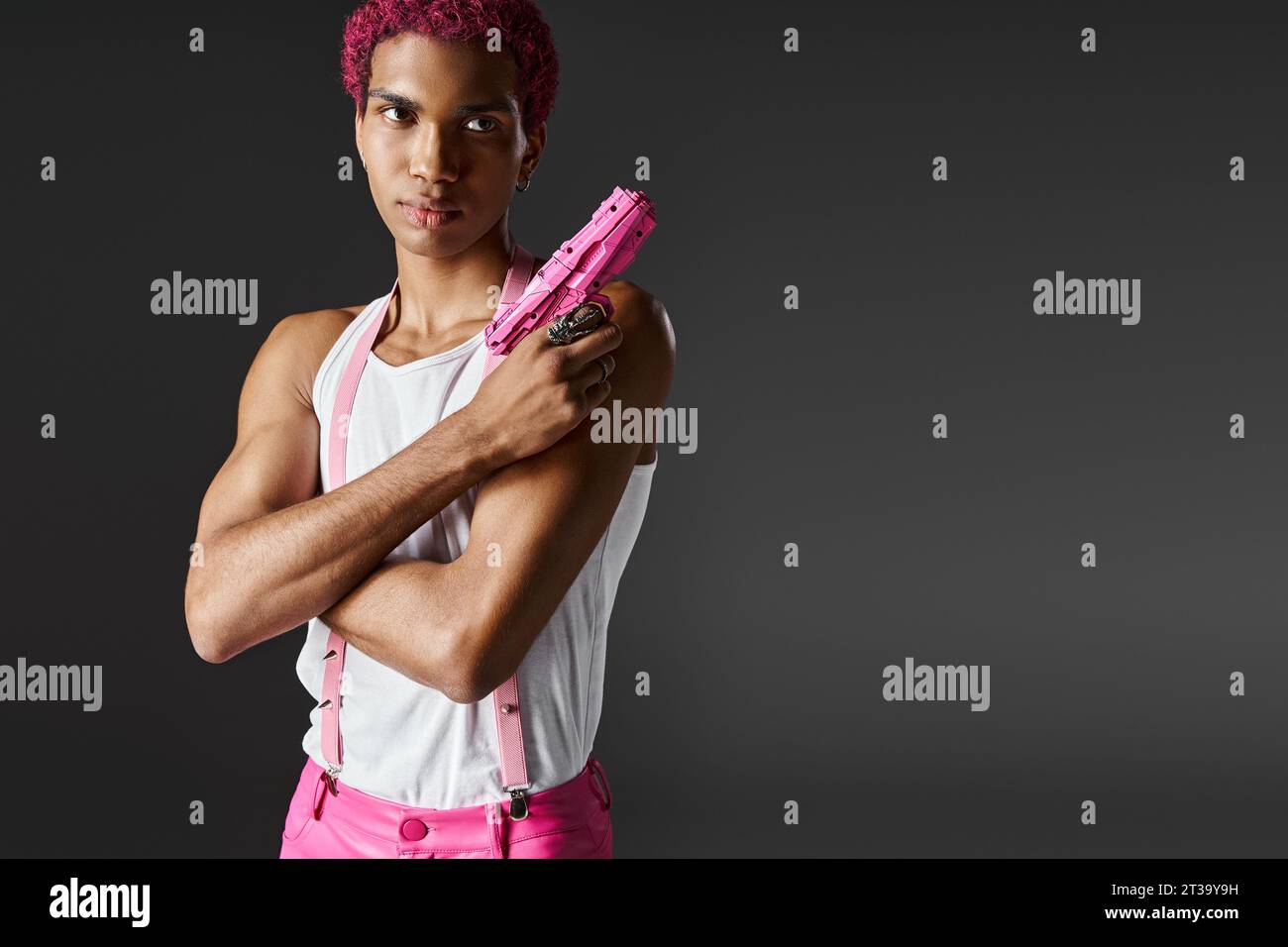 modèle masculin beau à la mode avec les cheveux roses posant avec pistolet jouet regardant sérieusement la caméra Banque D'Images