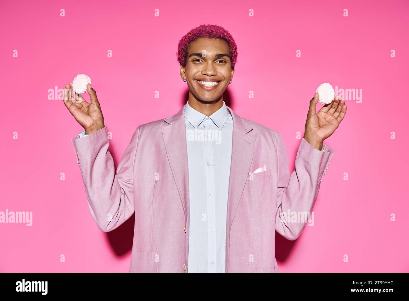 beau jeune modèle masculin souriant anormalement et tenant un délicieux zéfir dans les mains sur fond rose Banque D'Images