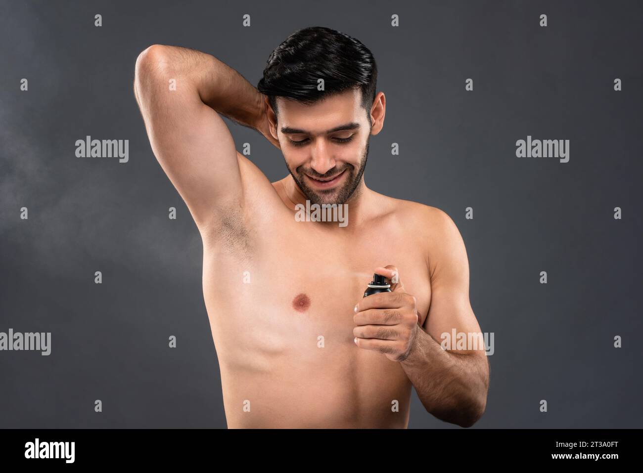 Torse nu bel homme caucasien utilisant un spray corporel déodorant en fond gris clair isolé photo de studio Banque D'Images