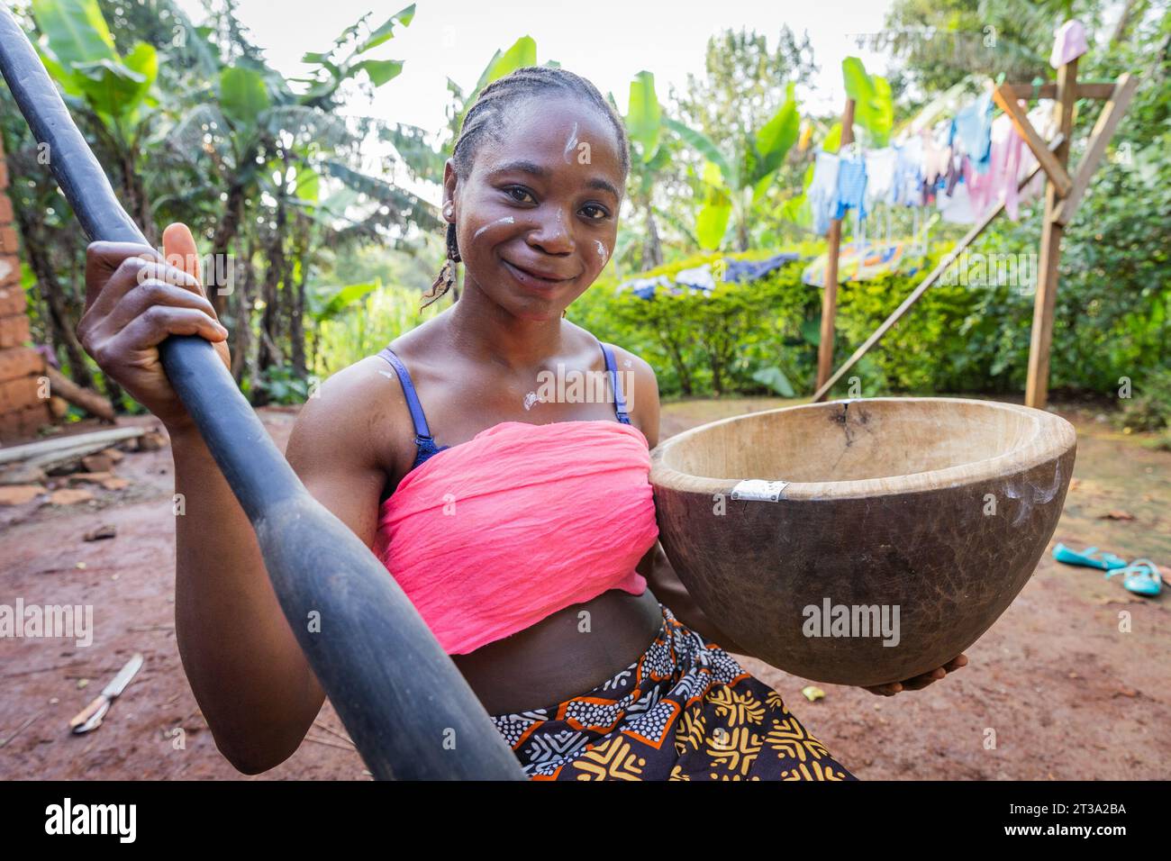 Souriante jeune femme villageoise africaine prête à battre un peu de glucides pour son repas de famille. Banque D'Images