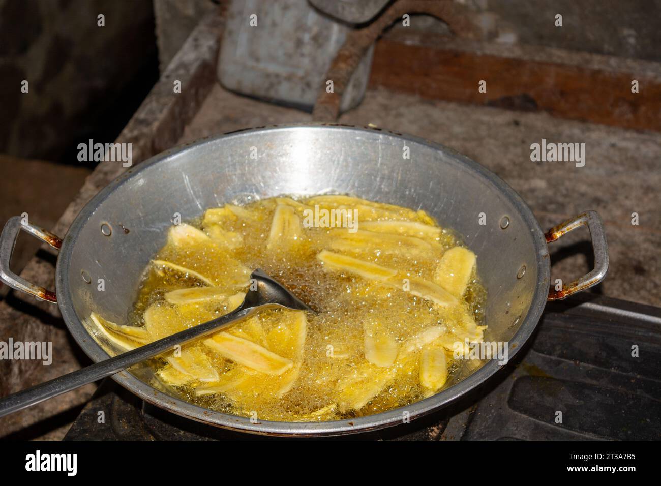 Le processus de friture des chips de banane avec de l'huile chaude, sur une grande poêle. Banque D'Images