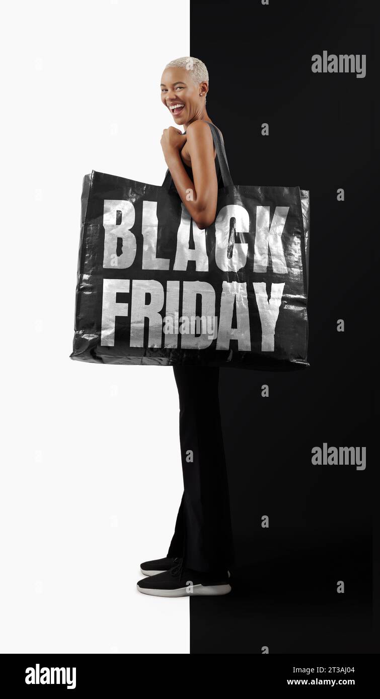 Black Friday Shopping. Superbe, joyeuse, souriante femme noire en tenue noire décontractée, tenant un grand sac shopper noir avec texte Black Friday écrit Banque D'Images