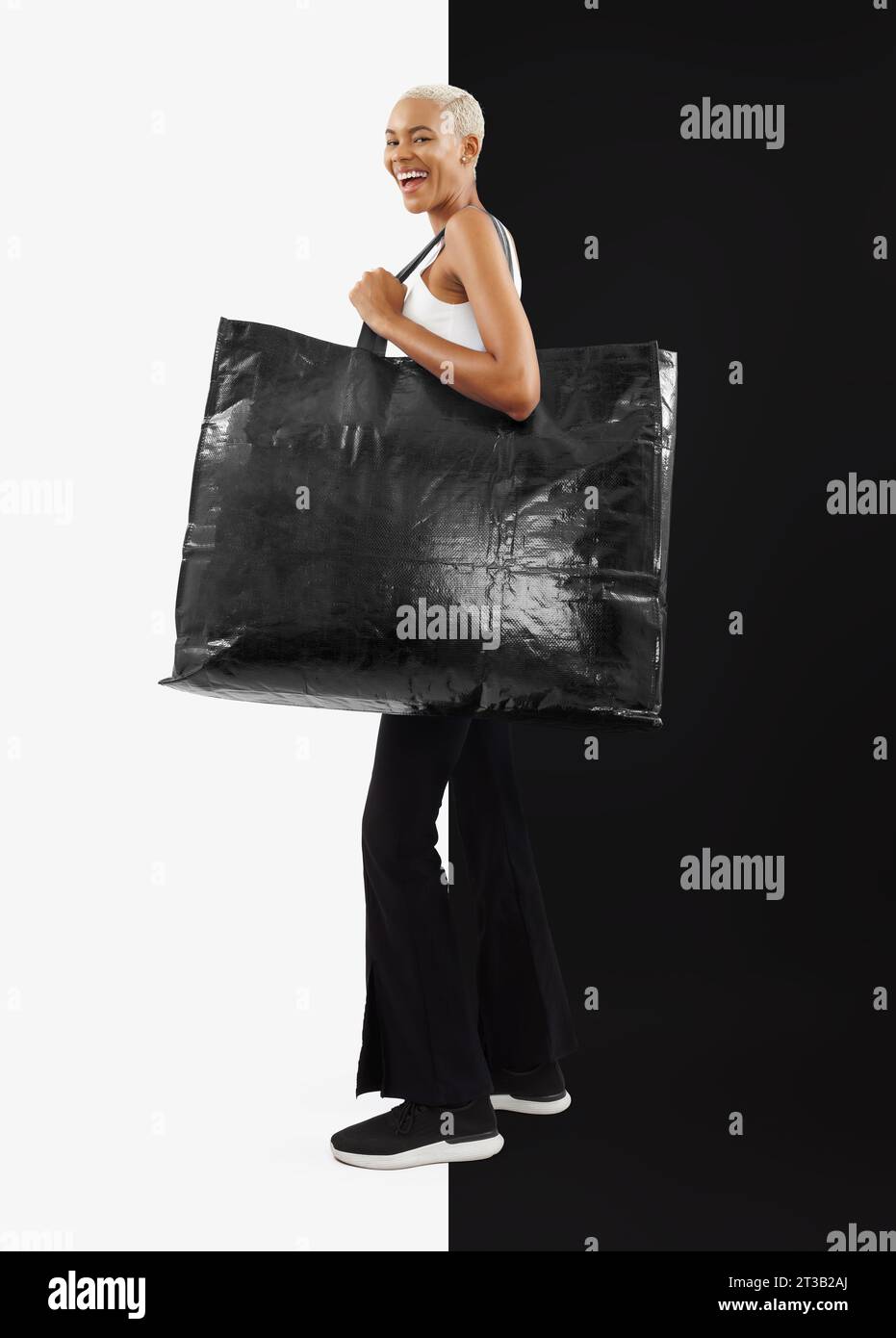 Black Friday Shopping. Femme noire riante, joyeuse et souriante dans une tenue décontractée, tenant un grand sac shopper noir avec espace de copie pour tex écrit Banque D'Images