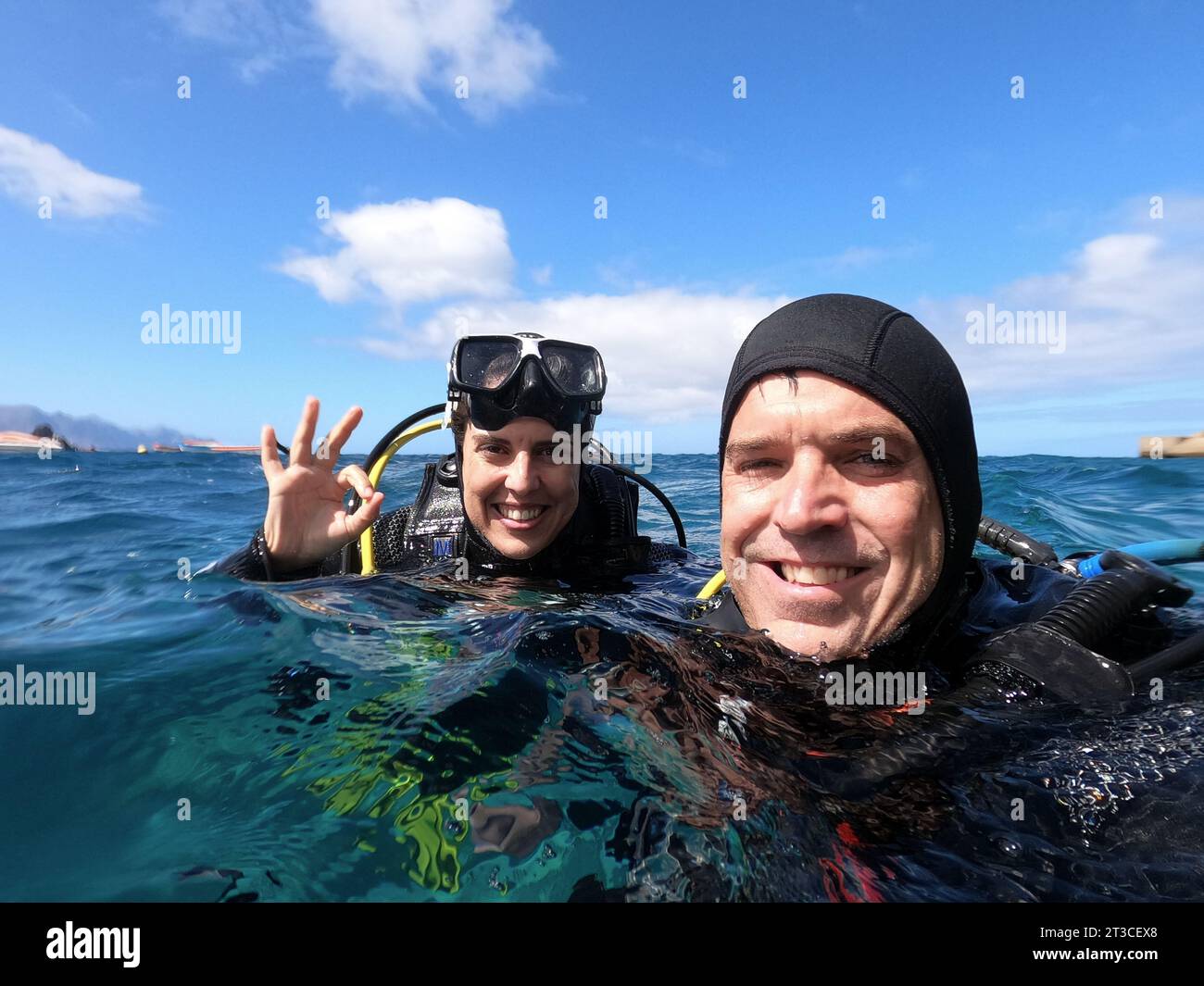 Couple, homme et femme, de plongeurs à la surface de la mer souriant faisant le signe 'OK' préparé pour une plongée sur une journée ensoleillée. Concept de sport nautique Banque D'Images