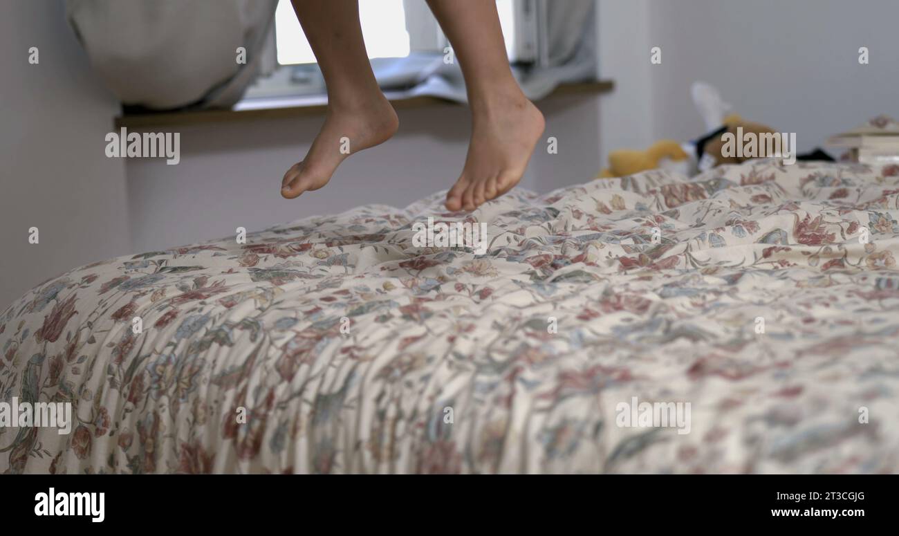 Les pieds de l'enfant sautant dans le drap de lit en super ralenti, les jambes de l'enfant atterrissant sur le lit jouant à la maison, concept de frissons capturé en 800 fps-SD Banque D'Images