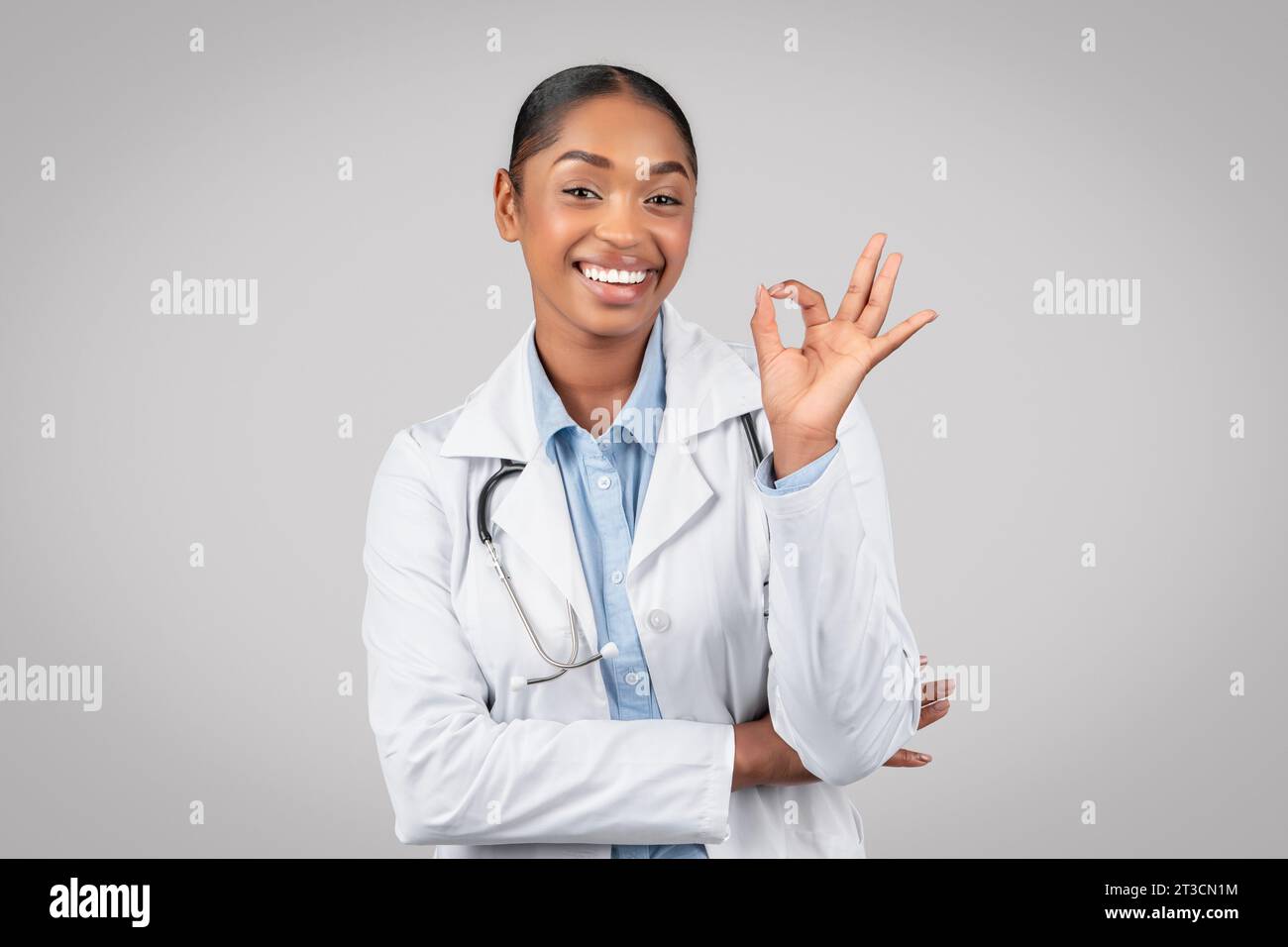 Glad jolie adulte femme afro-américaine médecin en manteau blanc faire signe ok avec la main Banque D'Images