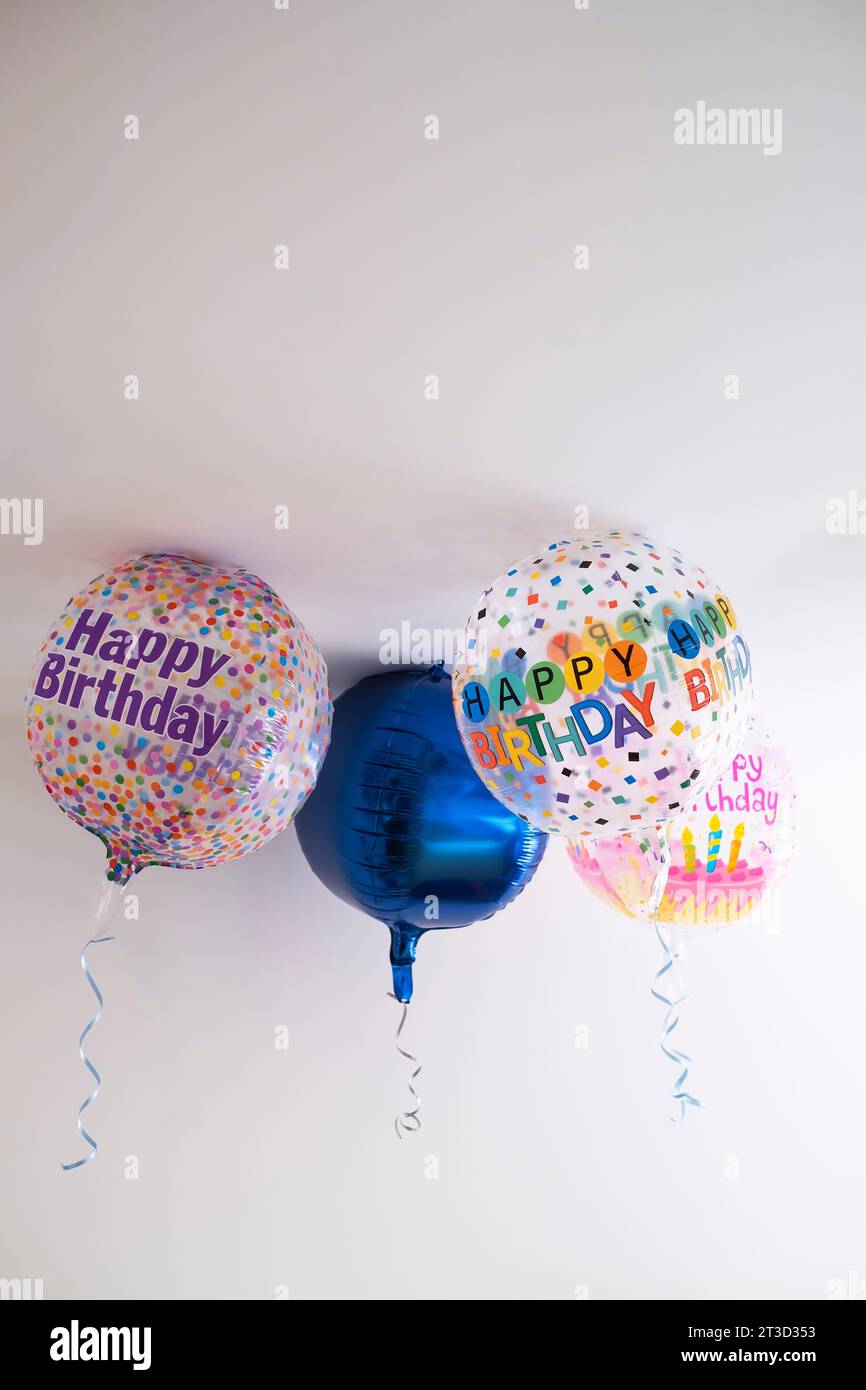 quatre ballons d'hélium décorés de points colorés et d'un message de joyeux anniversaire, avec un ruban suspendu, sur le toit d'une pièce blanche, fond dégradé Banque D'Images