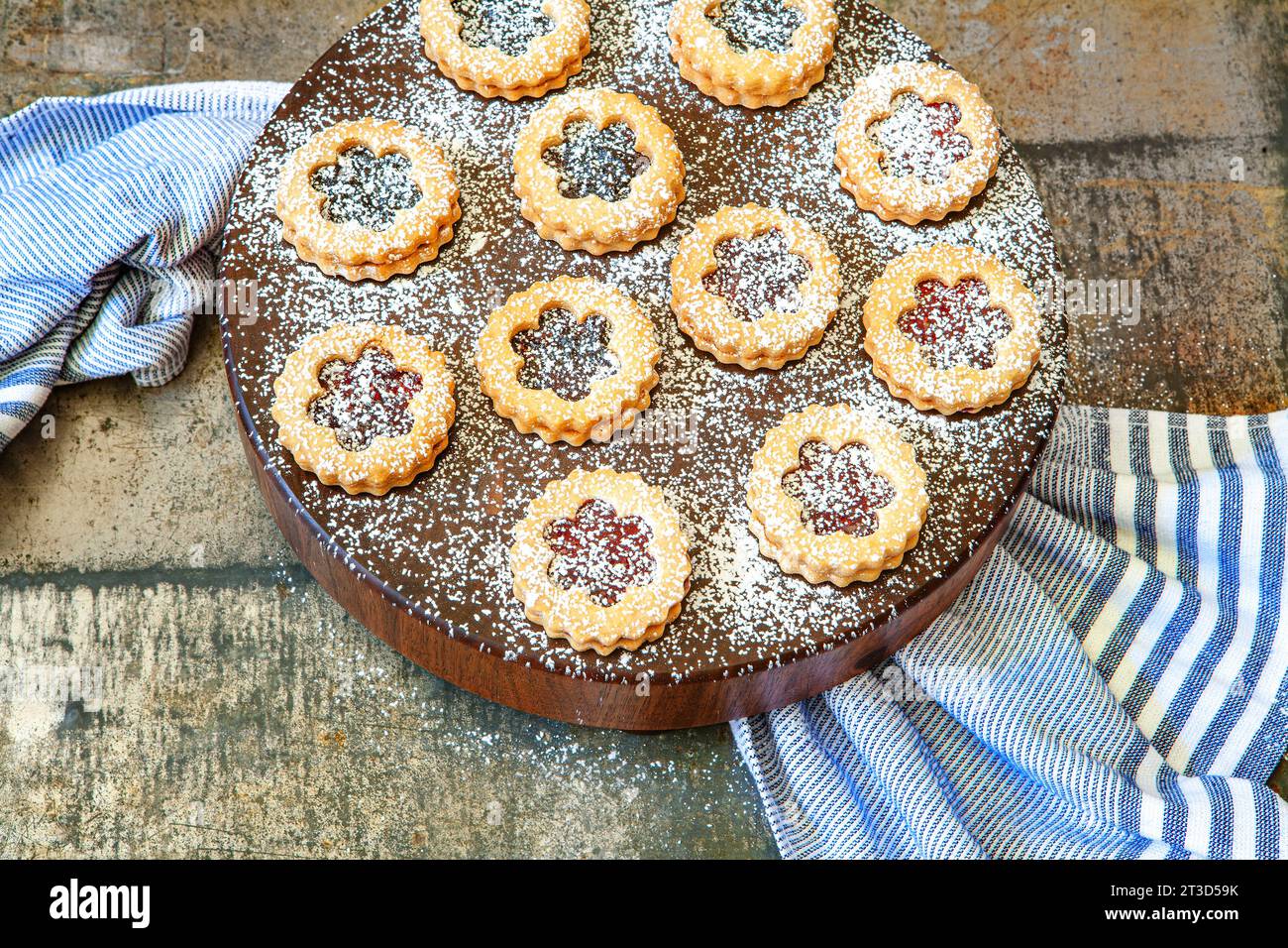 Vue à grand angle des tartes Linzer saupoudrées de sucre en poudre sur une planche de bois ronde avec une serviette bleue Banque D'Images