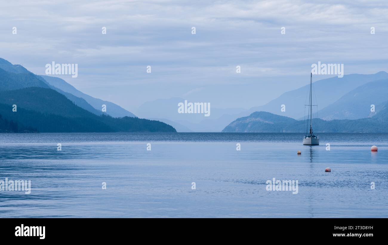 Un voilier est ancré à Sechelt Inlet sur la Sunshine Coast en Colombie-Britannique. Les montagnes entourent les eaux calmes du fjord. Banque D'Images