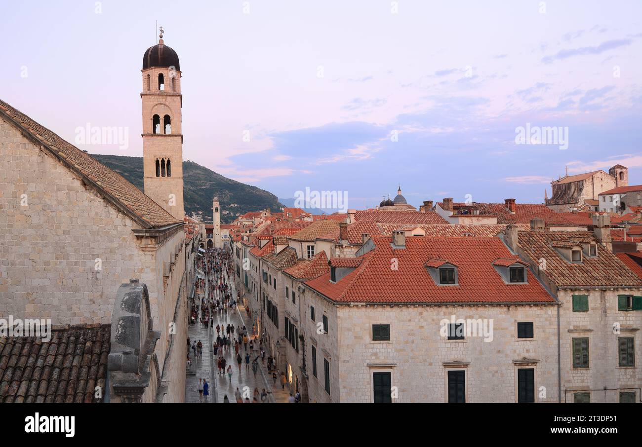 Touristes marchant sur l'ancienne rue Stradun dans la vieille ville de Dubrovnik au coucher du soleil, fond de ciel violet, Croatie Banque D'Images