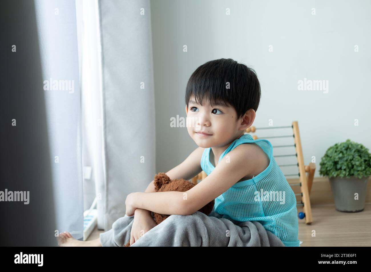 Garçon asiatique triste s'assied la tête baissée et regarde par la porte sa poupée préférée. Banque D'Images