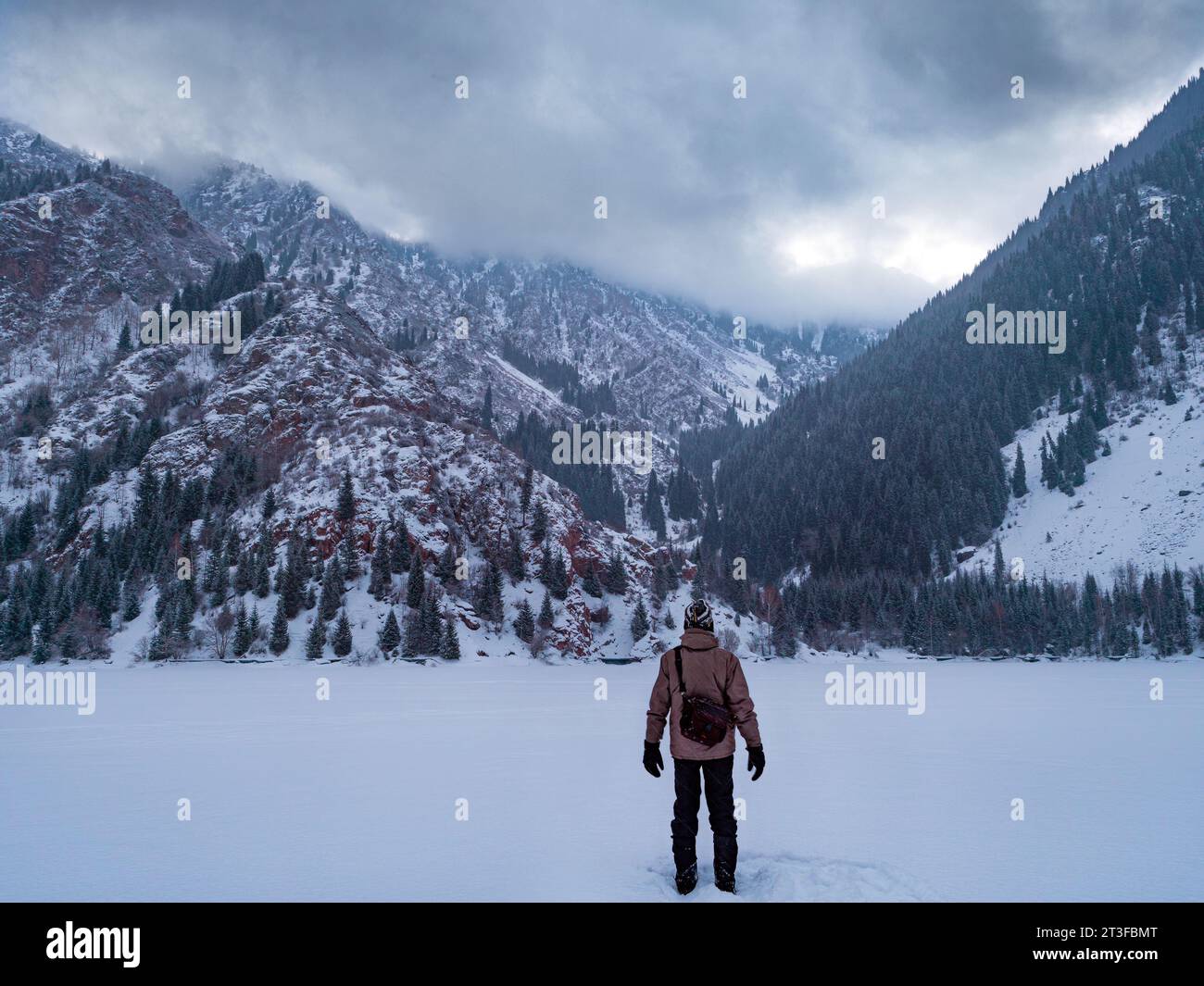 Un gars avec un appareil photo à la main dans une région montagneuse tard dans la nuit en hiver. Vue de l'arrière. Paysages de montagne hivernaux. Montagnes de neige ouverte Banque D'Images