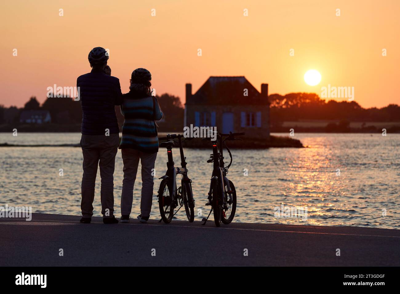 France, Morbihan, rivière Etel, Belz, couple à vélo devant l'îlot Nichtarguer et sa maison de pêcheur à SunsetBelzBelz Banque D'Images