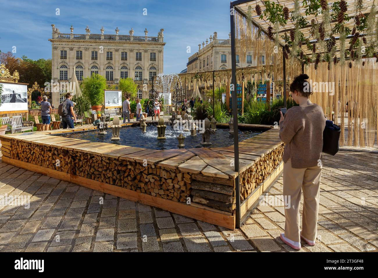 France, Meurthe et Moselle, Nancy, place Stanislas (ancienne place royale) construite par Stanislas Leszczynski, roi de Pologne et dernier duc de Lorraine au 18e siècle, classé au patrimoine mondial par l'UNESCO lors de l'événement jardin Ephemere 2023 qui célèbre le 40e anniversaire de l'inscription au patrimoine mondial de l'UNESCO et le 50e anniversaire du jumelage avec la ville japonaise de Kanazawa sur le thème de l'Air, femme tapant une image d'un jet d'eau et des façades de l'Opéra et du Grand Hôtel de la Reine en arrière-plan, photographies de Jacques Henri Lartigue Banque D'Images