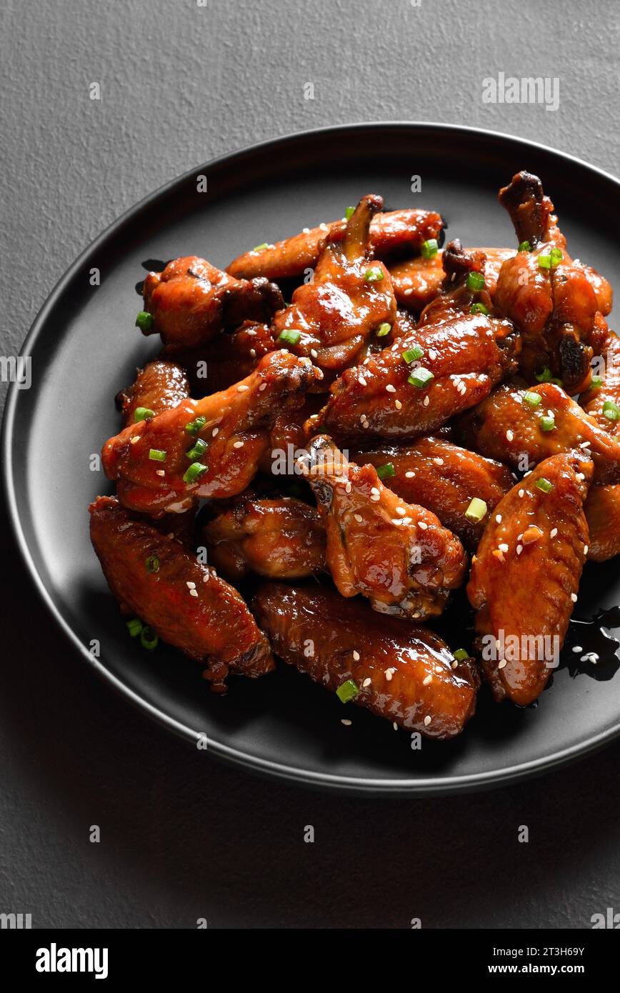 Ailes de poulet sucrées et épicées sur plaque sur fond de pierre sombre. Vue rapprochée Banque D'Images