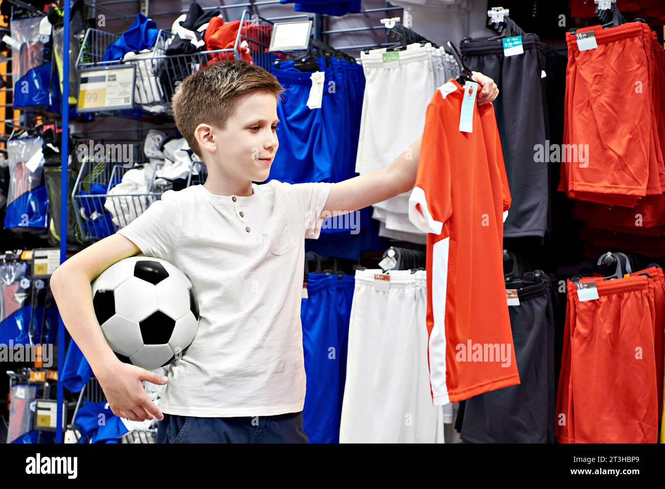 Garçon avec ballon de football et t-shirt rouge dans un magasin de vêtements de football Banque D'Images