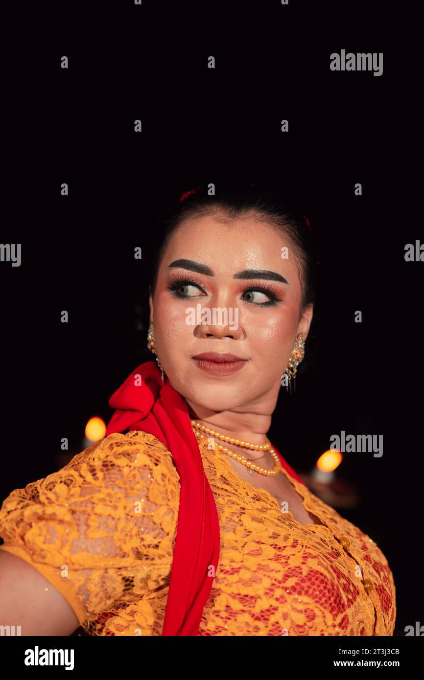 Femme javanaise dans une robe orange traditionnelle tout en portant le maquillage et une écharpe rouge à un festival de danse en Indonésie Banque D'Images