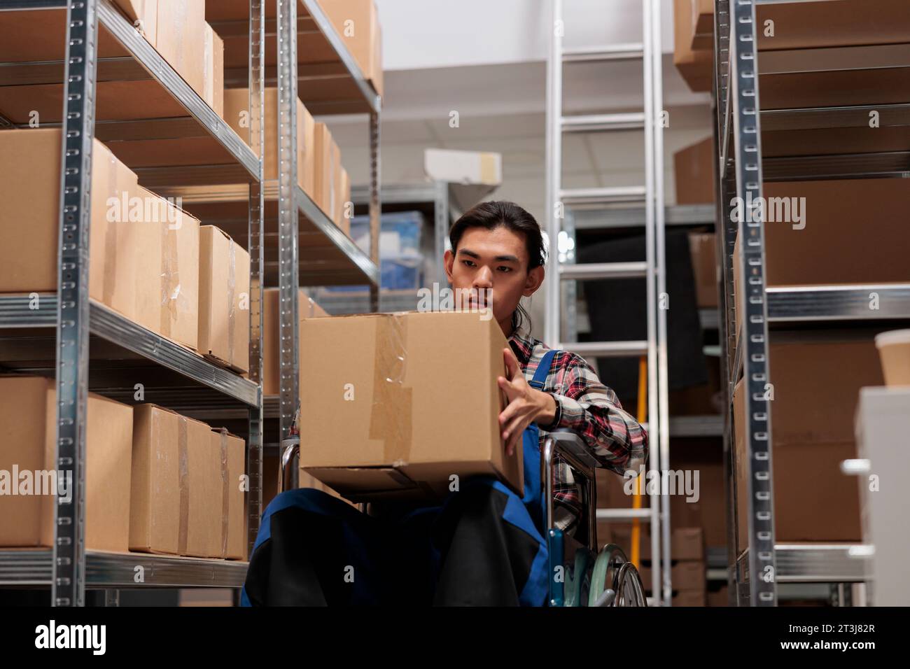 Gestionnaire de livraison de magasin en fauteuil roulant pour envoyer la commande du client. Entrepôt postal homme asiatique employé tenant la boîte en carton emballée tout en travaillant dans la salle de stockage adaptée aux personnes handicapées Banque D'Images