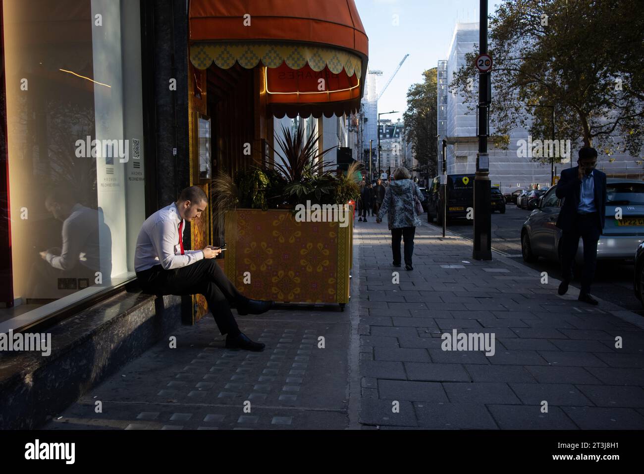 Employé d'hôtel prenant un moment solitaire assis dehors dans la lumière du soleil du soir pour prendre une pause de son horaire de travail, Berkeley Square, Londres, Angleterre Banque D'Images