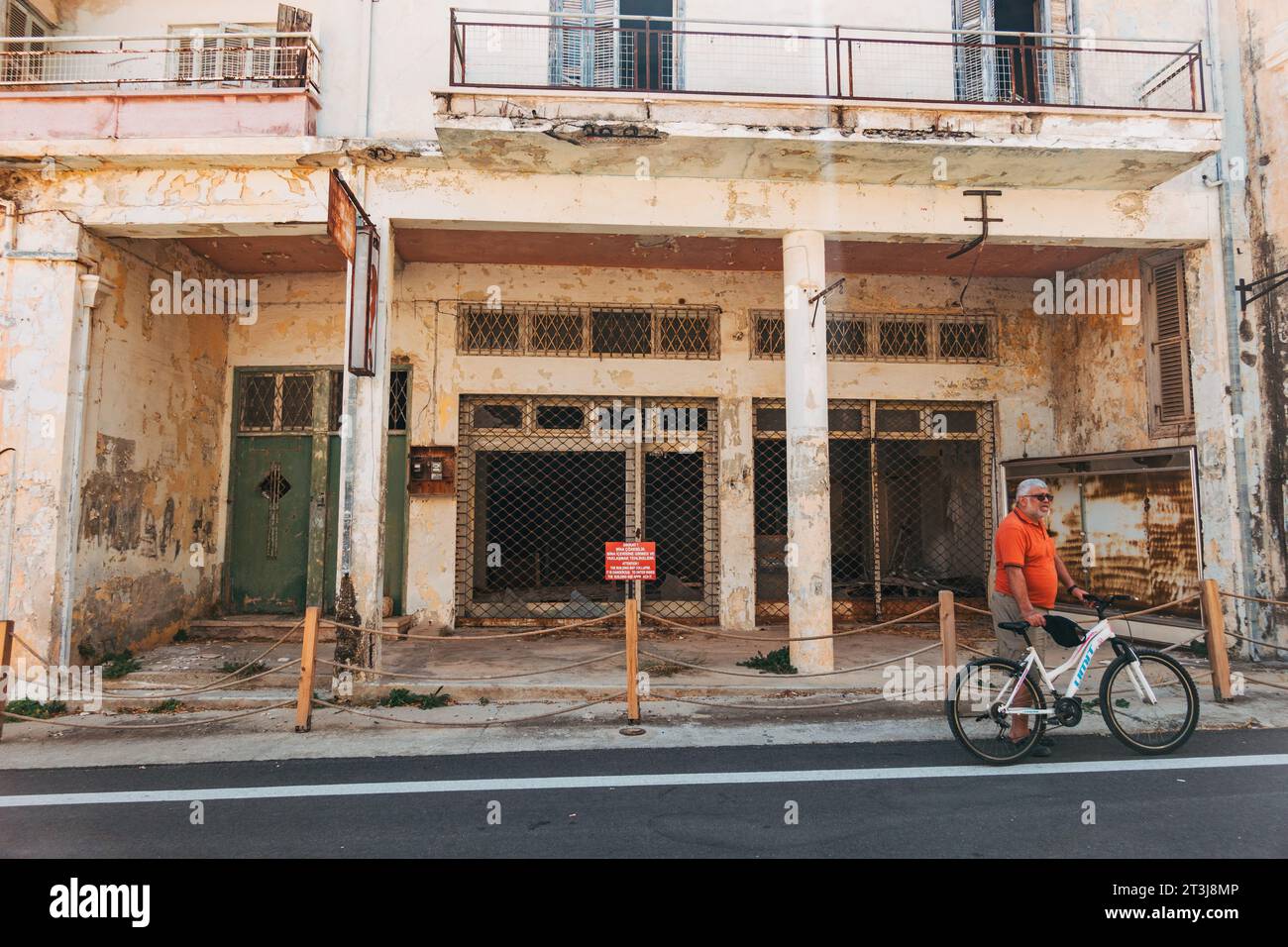 Un touriste à vélo visite la ville abandonnée de Varosha, Famagouste, Chypre. Un magasin vide peut être vu derrière Banque D'Images