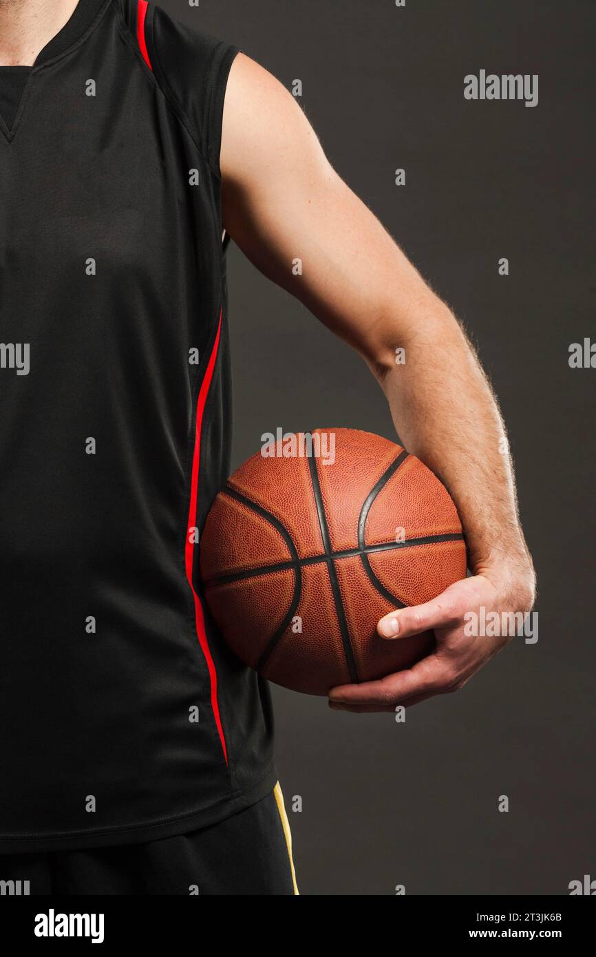 Ballon de basket-ball à vue de face tenu par le joueur près du corps Banque D'Images