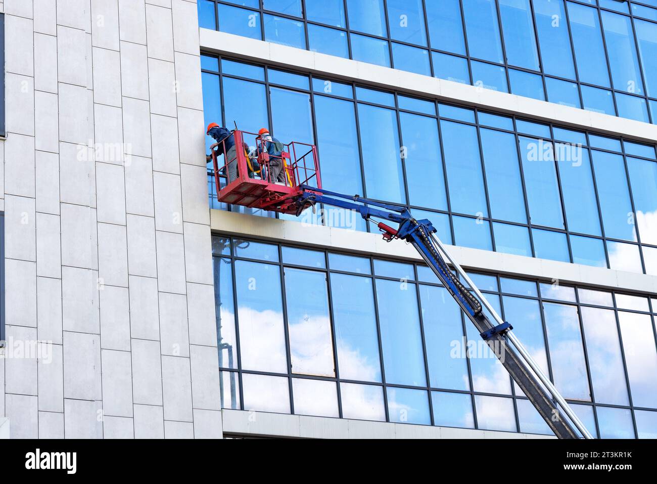 Les laveurs de fenêtre externes de façade en verre, tandis que dans un berceau de levage de construction, nettoient la façade en verre d'un bâtiment par temps clair. Banque D'Images