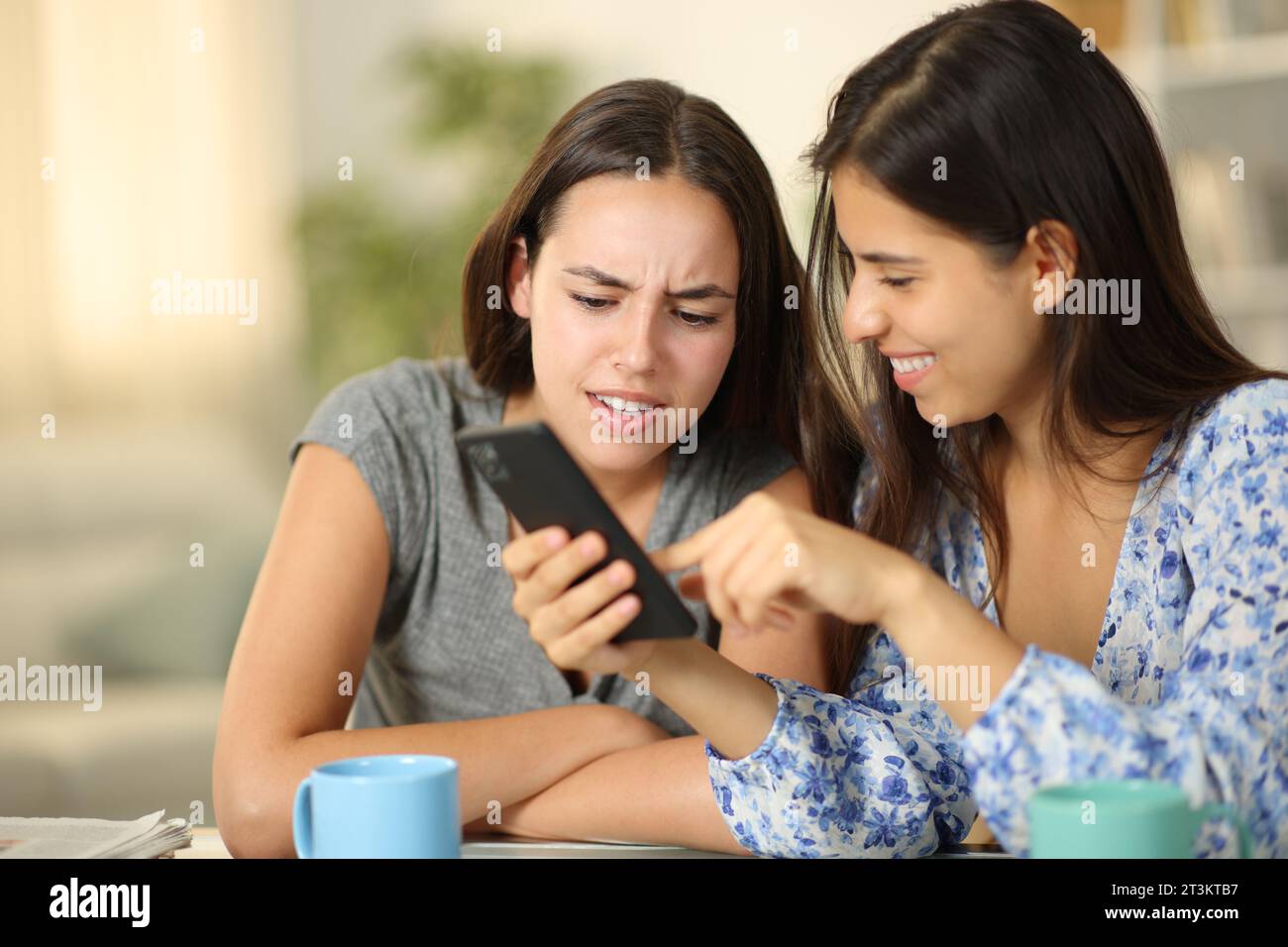 Deux amis regardant du contenu multimédia drôle sur le téléphone à la maison Banque D'Images