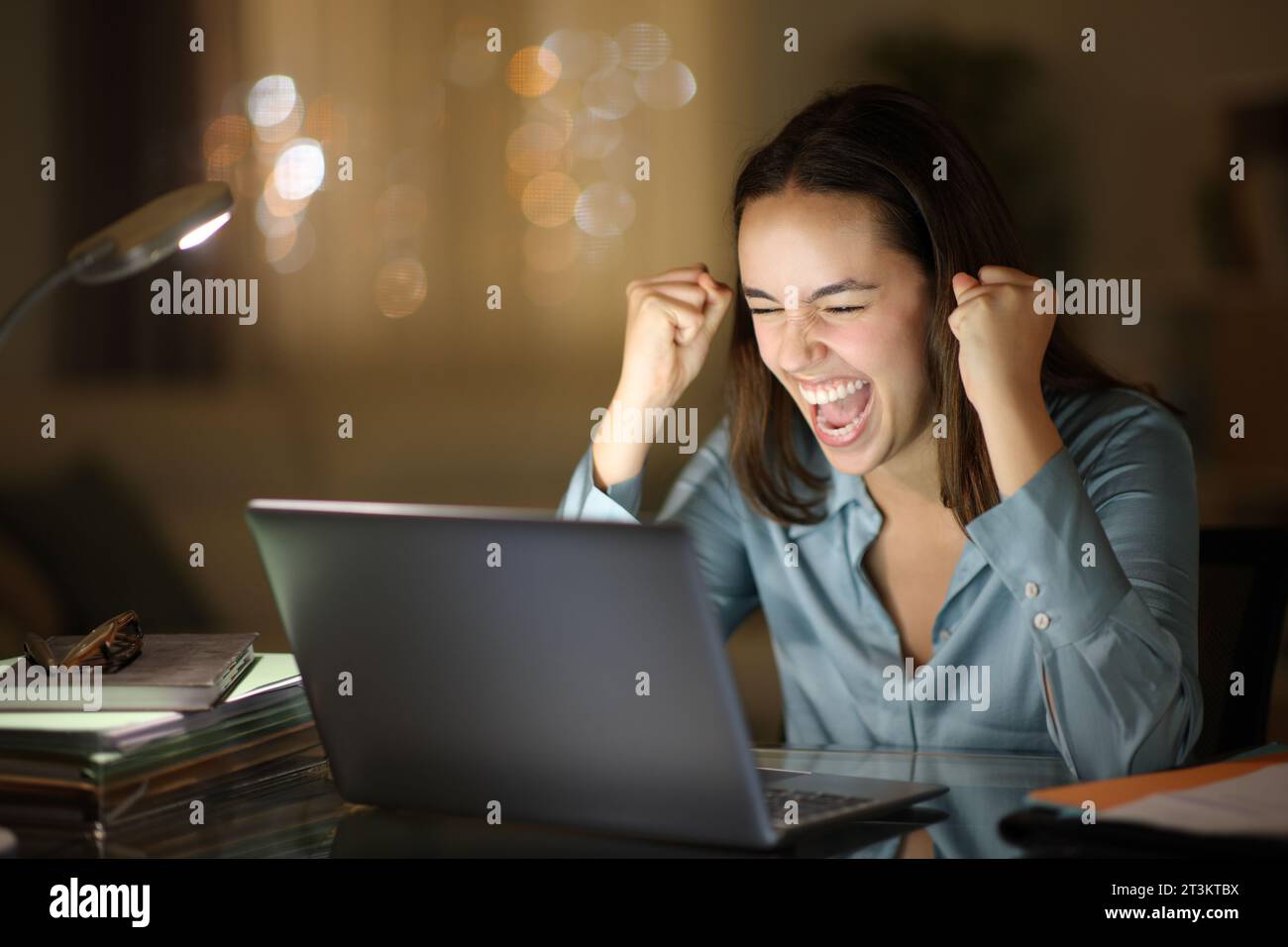 Travailleur excité qui vérifie le contenu d'un ordinateur portable et qui fête en ligne la nuit au bureau à domicile Banque D'Images