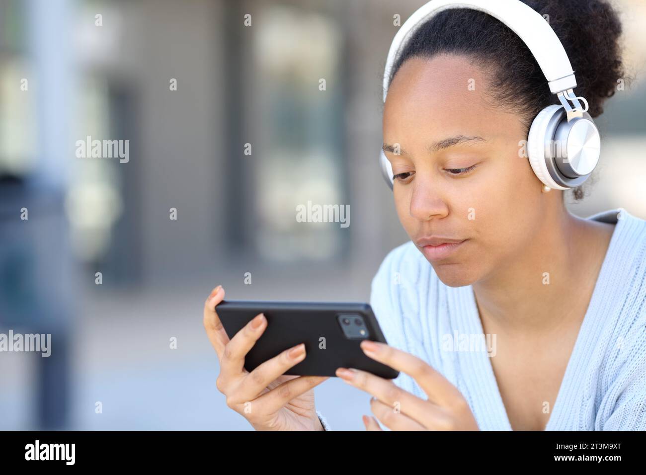 Femme noire avec casque regardant la vidéo en ligne sur le téléphone dans la rue Banque D'Images