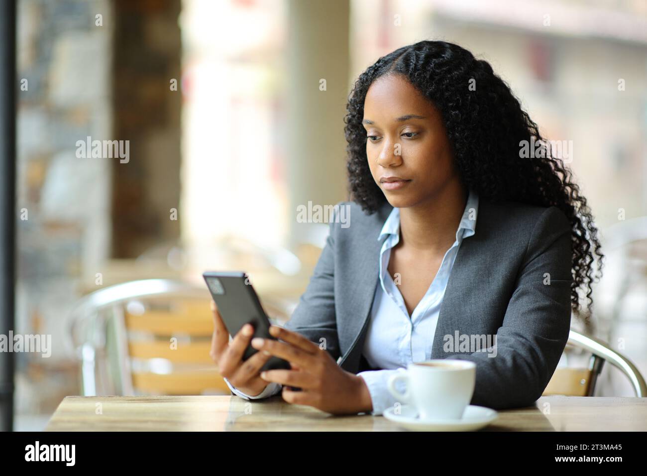 Femme d'affaires noire sérieuse utilisant le téléphone assis dans une terrasse de bar Banque D'Images