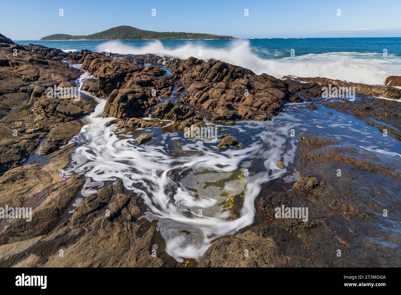 Les vagues s'écrasent sur une côte sauvage et tourbillonnent dans les piscines rocheuses de Fingal Bay en Nouvelle-Galles du Sud, en Australie Banque D'Images