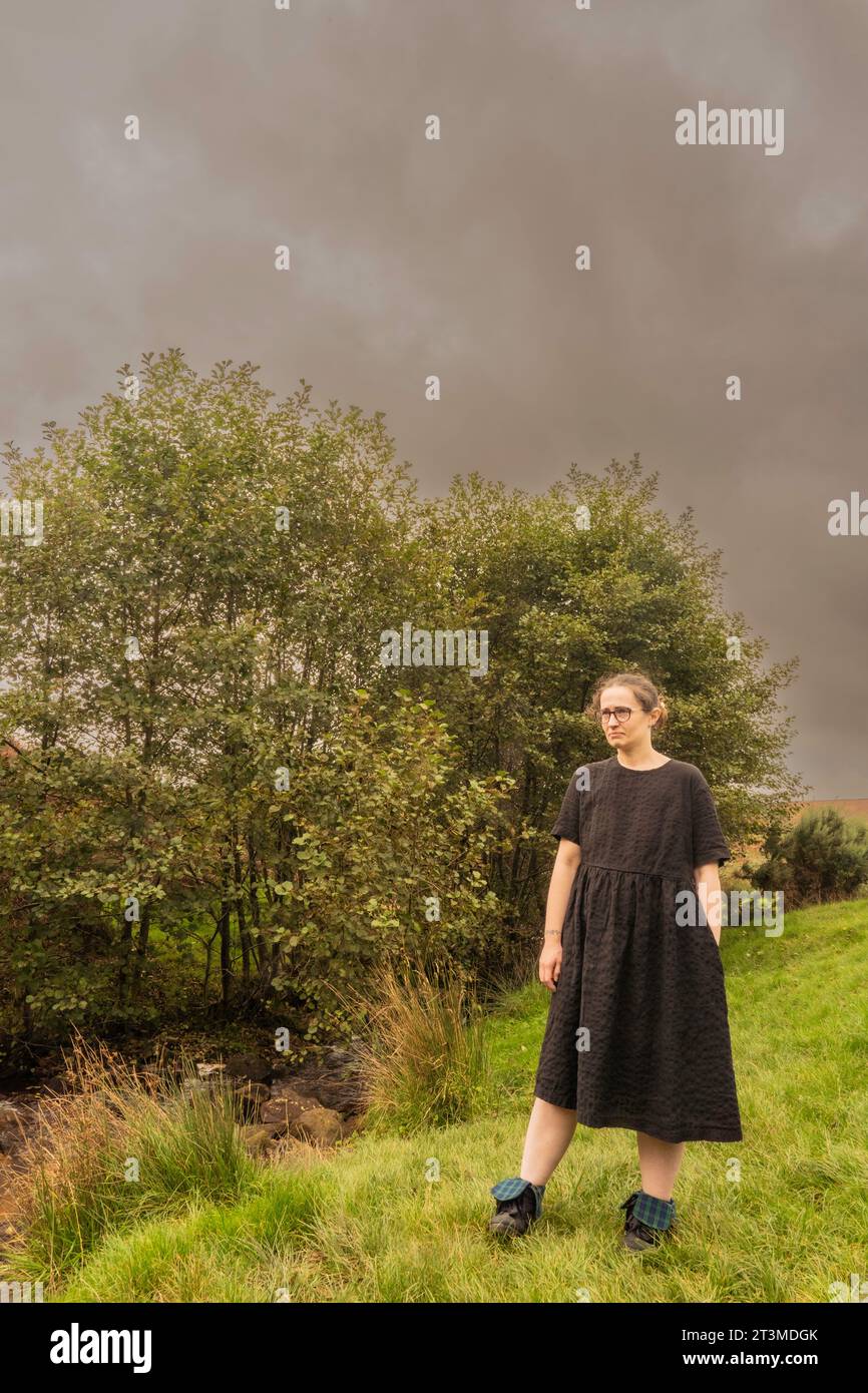 Fille solo en robe noire et lunettes debout près de quelques buissons à Osmotherly, North Yorkshire, Angleterre, Royaume-Uni Banque D'Images